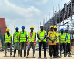 Group of workers in safety gear at a construction site. Visible scaffolding and clear sky.