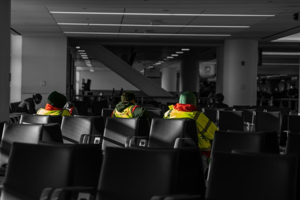 Three people in yellow vests sit in airport chairs.